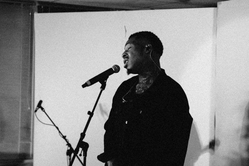 Singer-songwriter Obii is photographed in a creative portrait setup, wearing a black turtleneck, captured in a moment of artistic expression with soft studio lighting. 