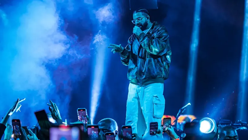 Drake performing on stage under dramatic concert lighting.