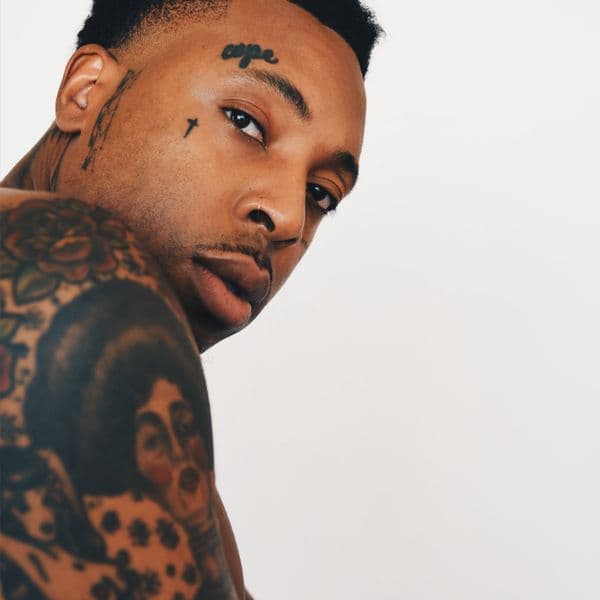 Singer-songwriter Obii poses for a portrait photograph, wearing a black turtleneck against a neutral background, looking directly at the camera with a contemplative expression.